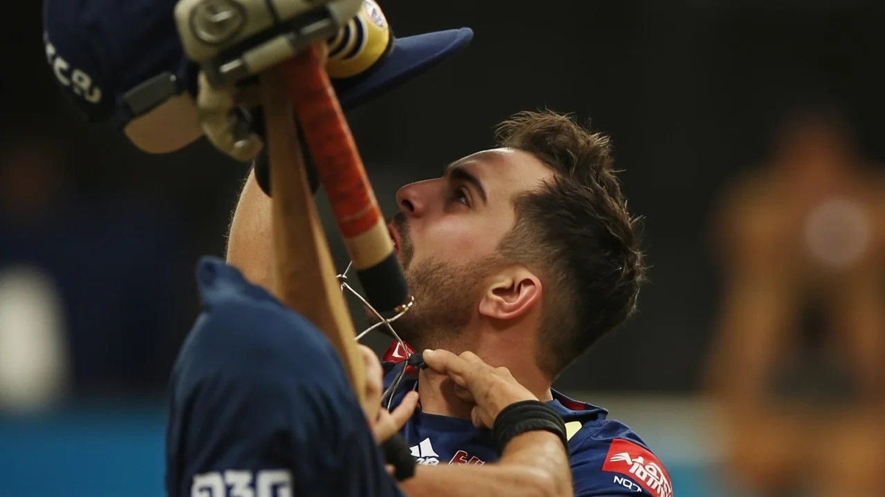 A cricket batter in batting stance under stadium lights during a T20 match